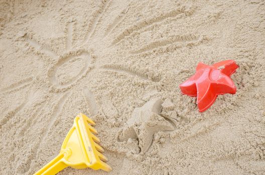 Sun drawn in sand on a sandy beach. With summer toys.