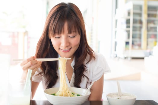 Eating noodles at restaurant. Young Asian girl eating ramen noodles using chopsticks.