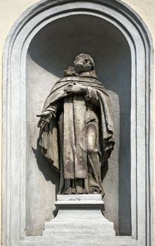 statue of a priest in front a castle walls 