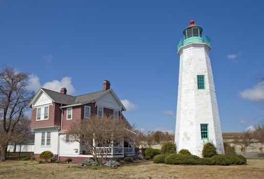 The Old Point Comfort lighthouse, a part of the new Fort Monroe National Monument, with the keepers quarters in winter against a bright blue sky with white clouds