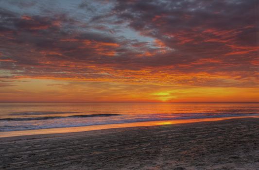 Dramatic clouds mask the sun as it rises over the Atlantic ocean to illuminate the sandy beach at Nags Head on the Outer Banks of North Carolina