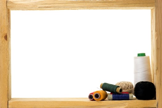 Spools with colored sewing thread inside rough wooden frame on white background 