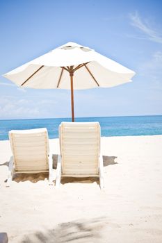 Two chairs under an umbrella on a beautiful sandy empty beach, rear view