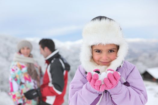 Little girl playing in the snow with her parents