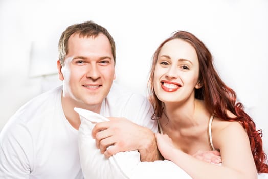 Young man and woman lying together in bed, smiling and happy