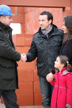 Architect shaking hands with a young family on site