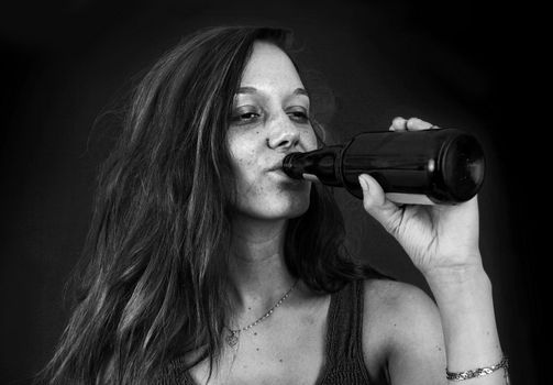 Dramatic black and white portrait of drunk young woman drinking beer over black
