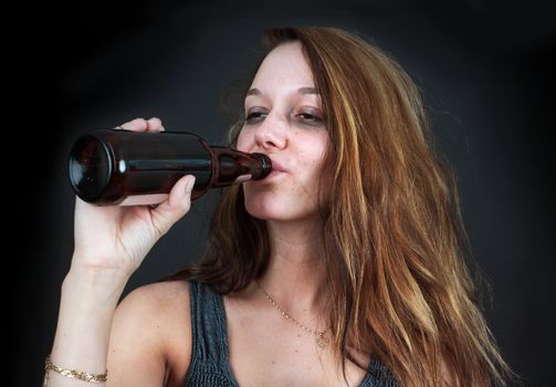 Portrait of drunk young woman drinking beer over black