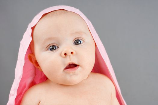 Portrait of a suprised newborn baby girl with pink blanket on her head