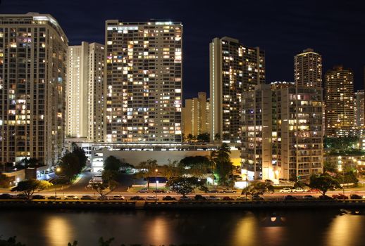 Office buildings and apartments form a partial skyline of Honolulu along the Ala Wai Canal near the Hawaii Convention Center at night