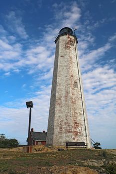 The Five Mile Point Light in New Haven, Connecticut, against a dramatic blue sky and white clouds vertical.  The lighthouse was built in 1847 and is 70 feet tall.  It is accesible through Lighthouse Point Park.