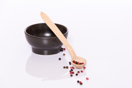 Black and rose pepper in wooden spoon and in black bowl