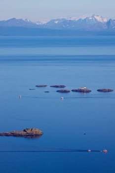 Lighthouse on tiny rocky islets near Lofoten islands with mountainous norwegian coast in the background