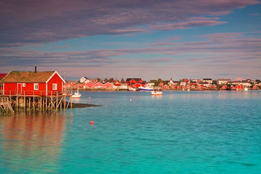 Typical red rorbu hut with sod roof in town of Reine on Lofoten islands in Norway lit by midnight sun
