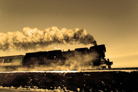 Vintage steam train puffing through countryside during wintertime
