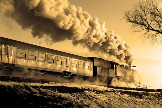 Vintage steam train puffing through countryside during wintertime
