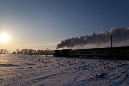 Vintage steam train puffing through countryside during wintertime
