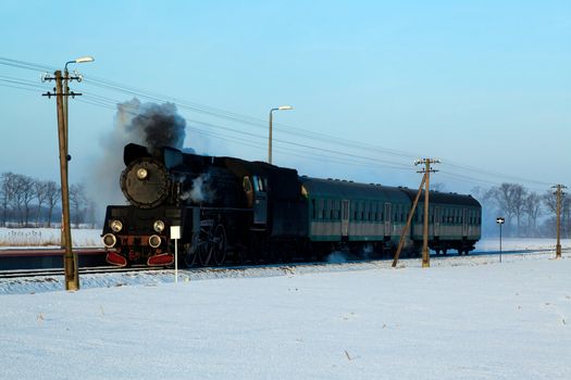 Vintage steam train puffing through countryside during wintertime
