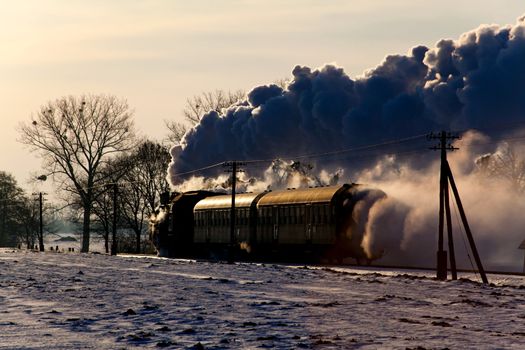 Vintage steam train puffing through countryside during wintertime
