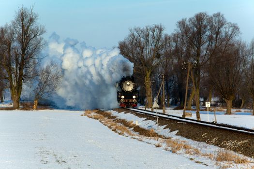 Vintage steam train puffing through countryside during wintertime
