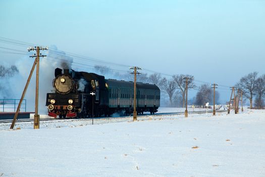 Vintage steam train puffing through countryside during wintertime
