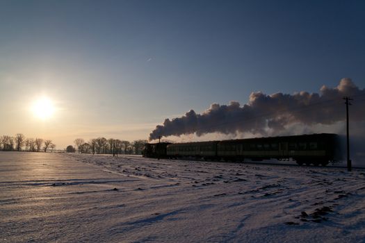 Vintage steam train puffing through countryside during wintertime
