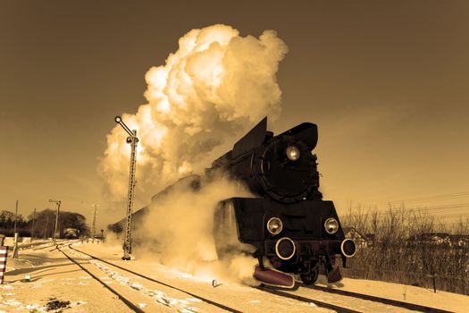 Vintage steam train puffing through countryside during wintertime
