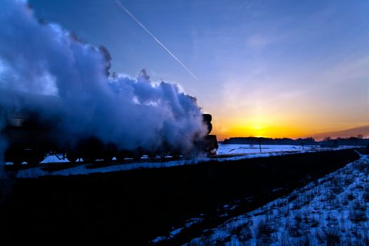 Vintage steam train puffing through countryside during wintertime
