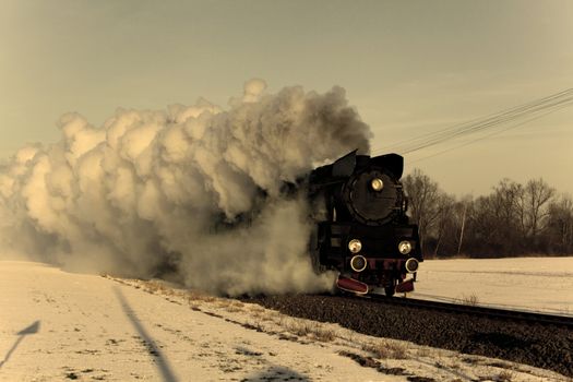 Vintage steam train puffing through countryside during wintertime
