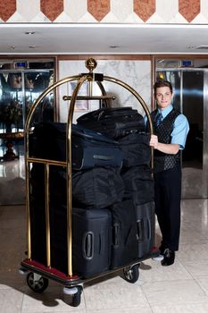 Bell boy pushing cart loaded with luggage to the guests room