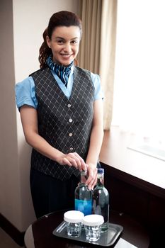 Cheerful waitress opening bottle of beverage, ready to be served