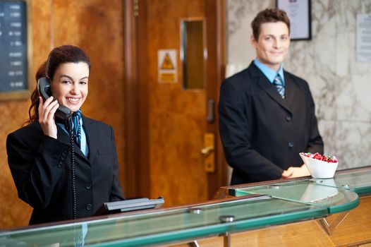 Profile shot of attractive executives at the reception of a hotel. Woman attending phone call