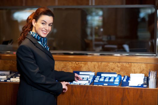 Front office female assistant checking customer records at work. Looking at camera