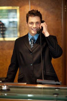 Cheerful front desk executive attending phone call while looking at camera