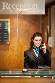 Attractive young receptionist in formal attire receiving calls and greeting customers with a smile