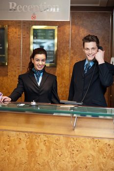 Male and female at hotel reception busy working. Man attending phone call