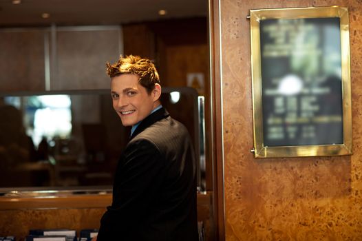 Attractive young guy turning back and looking at you. Indoors reception shot