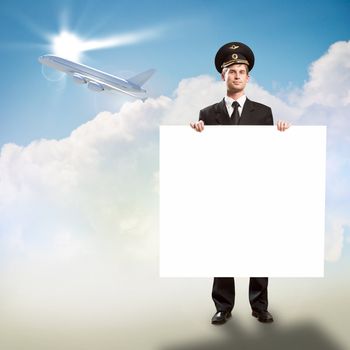 pilot in the form of holding an empty billboard on the background of sky and flying plane, place for text