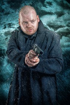 Armed man with a handgun wearing a heavy winter overcoat in a dark cold environment holding his gun at the ready, conceptual of either terrorism, crime or law enforcement