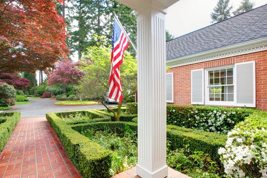 American old brick home with flag and classic garden during spring.