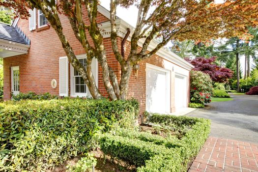 Brick classic detached garage building with two white doors and maple.