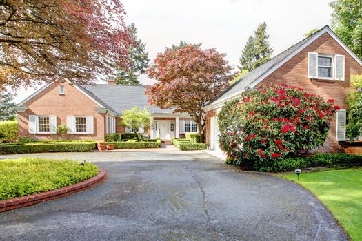 Brick red house with English garden and white window shutters. Summer landscape.