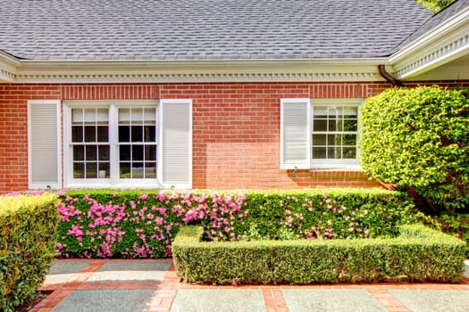 Brick red house with English garden and white window shutters. Summer landscape.