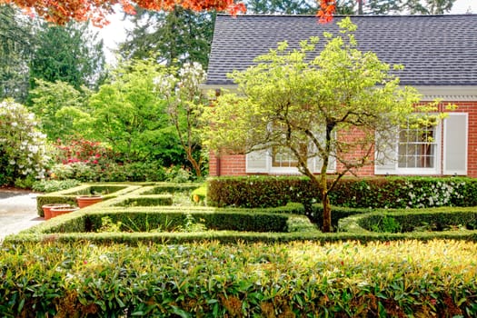 Brick red house with English garden and white window shutters. Summer landscape.