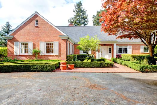 Brick red house with English garden and white window shutters. Summer landscape.