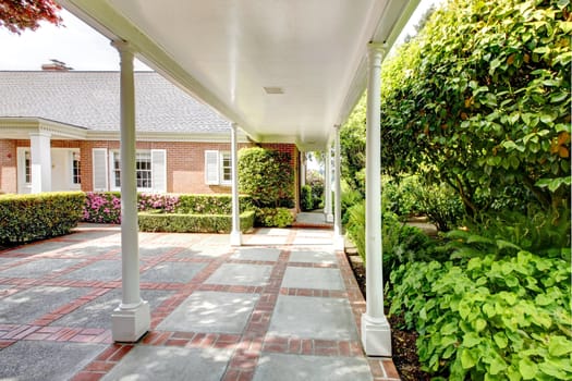 Brick red house with English garden and white window shutters. Summer landscape.