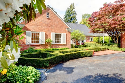 Brick red house with English garden and white window shutters. Summer landscape.