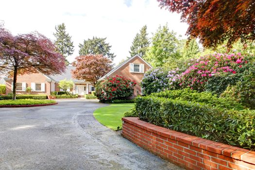 Brick red house with English garden and white window shutters.  Long driveway with Summer landscape.