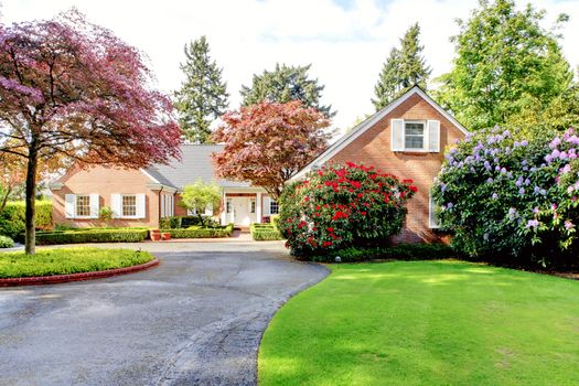 Brick red house with English garden and white window shutters. Summer landscape.