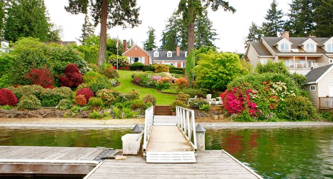 Brick red house with English garden and white window shutters. Summer landscape.